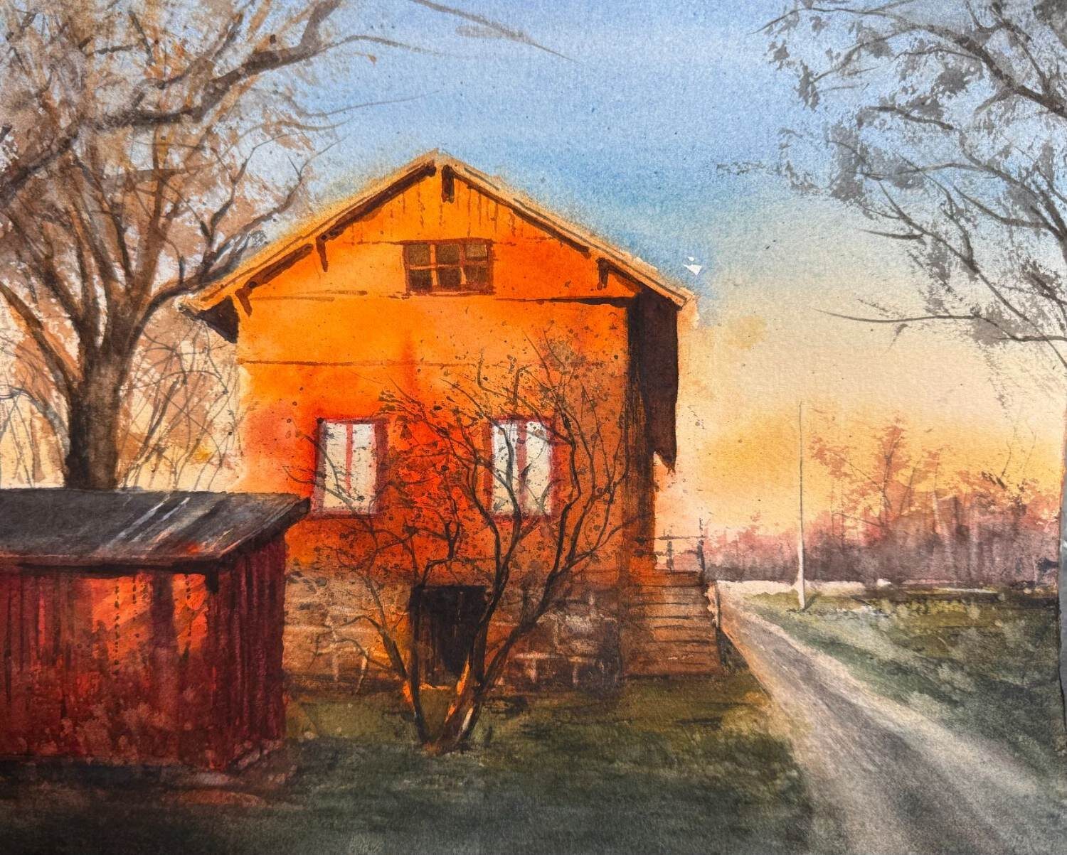 Rött hus och väg i låg vintersol med kala träd.