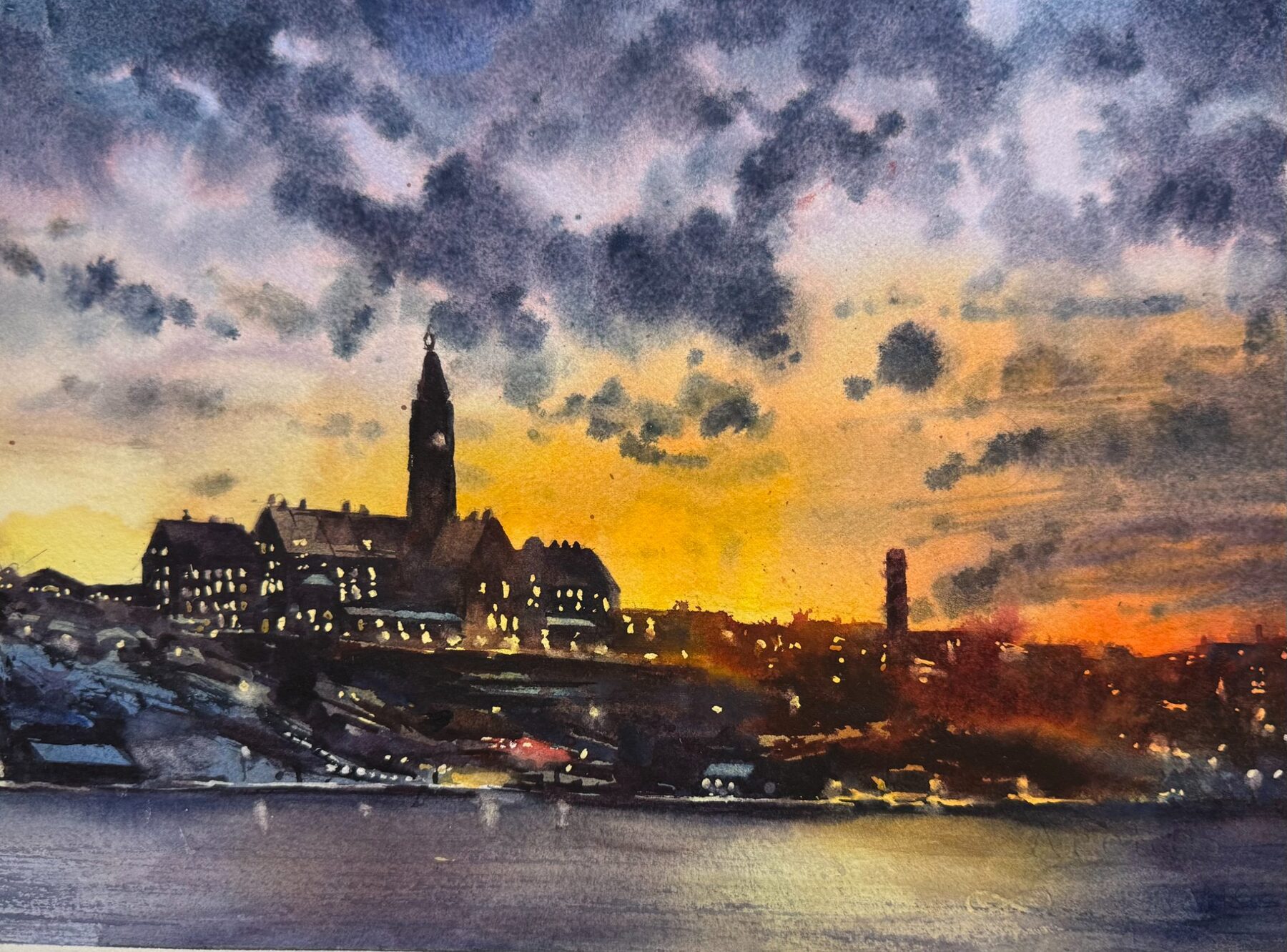 Stadsvy över Danviken i skymning med mörka moln och upplyst torn.