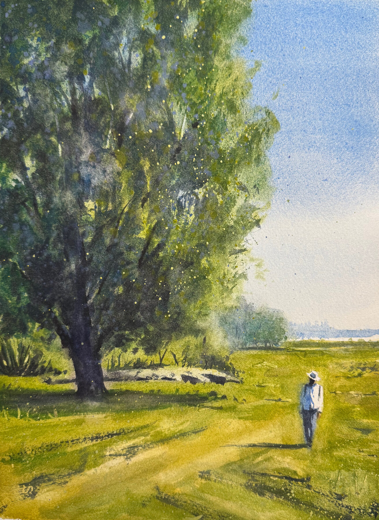 Gestalt i vitt på stig genom grön sommaräng vid träd.